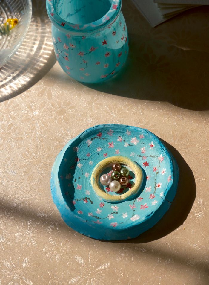 product-04 A handmade blue clay dish with floral patterns, featuring colorful beads inside, under warm lighting.