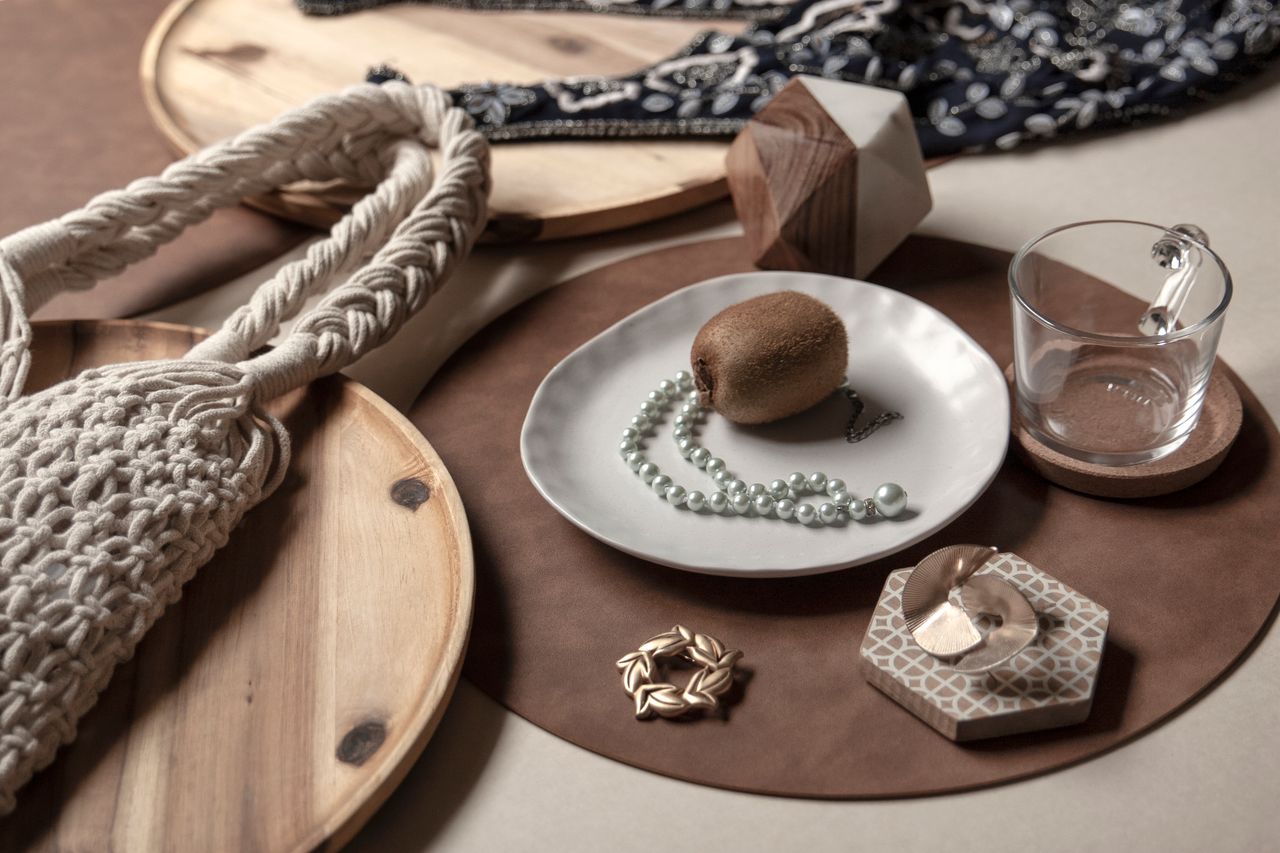 About Beautiful arrangement featuring kiwi, ceramic plate, jewelry, and accessories on wooden backdrop.